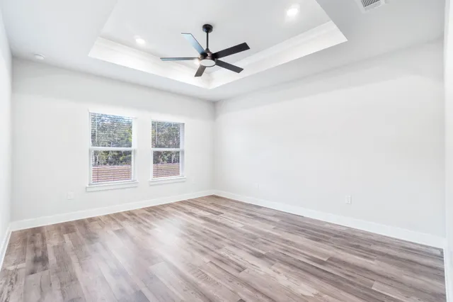 an empty room with wooden floor ceiling fan and windows