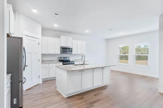 a kitchen with stainless steel appliances granite countertop a stove a refrigerator a sink and white cabinets with wooden floor