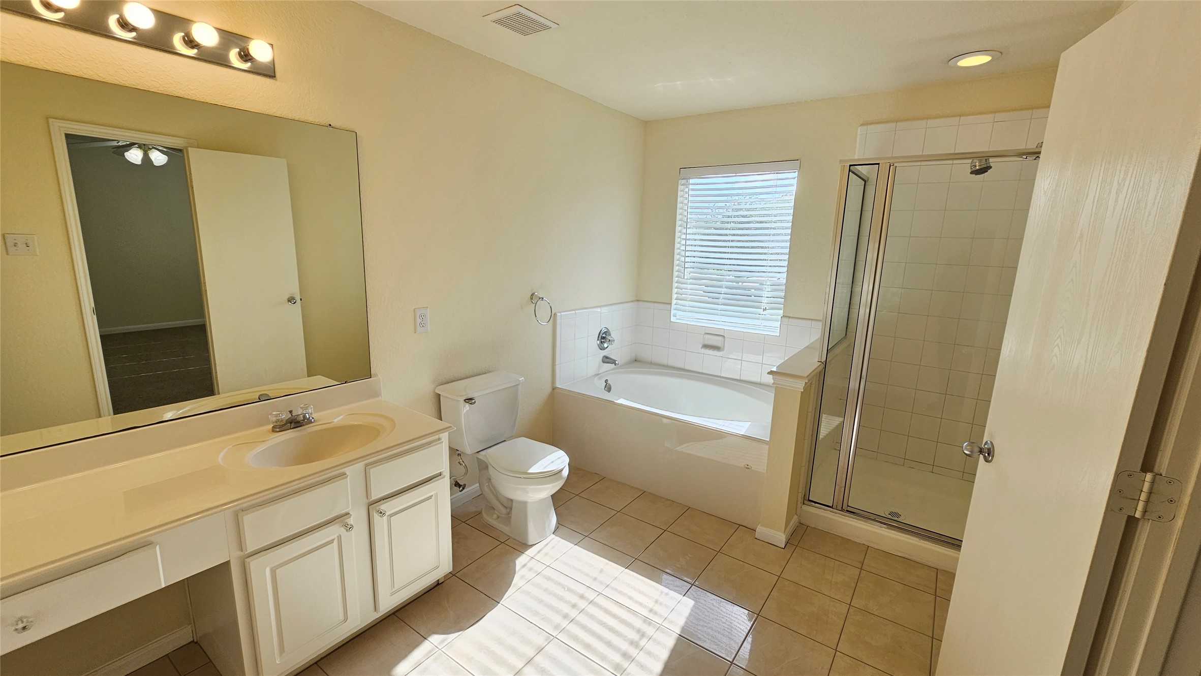 7918 Barnes Ridge Lane Houston, TX 77072 - Photo 25 of 34 This bright bathroom features a large vanity with ample storage, a spacious bathtub with a window above, a separate glass-enclosed shower, and neutral tile flooring, creating a clean and airy feel.