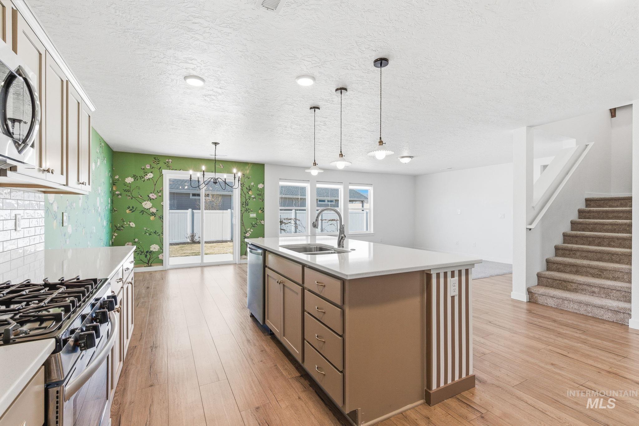 110 Homesteaders Street Middleton, ID 83644 - Photo 11 of 49 Kitchen with light wood-style flooring, stainless steel appliances, wallpapered walls, a kitchen island with sink, and a textured ceiling