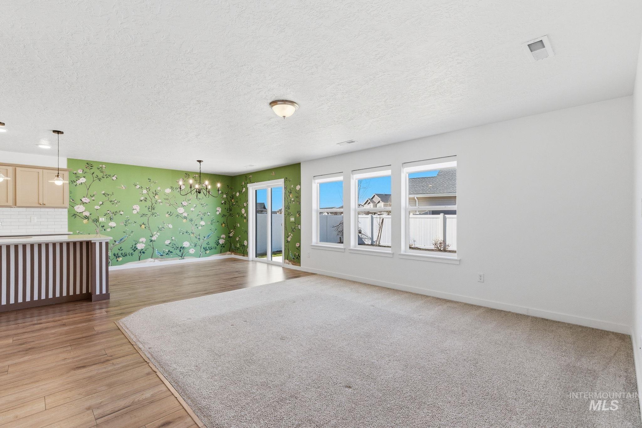 110 Homesteaders Street Middleton, ID 83644 - Photo 4 of 49 Unfurnished living room featuring a chandelier, wallpapered walls, a textured ceiling, light wood finished floors, and an accent wall
