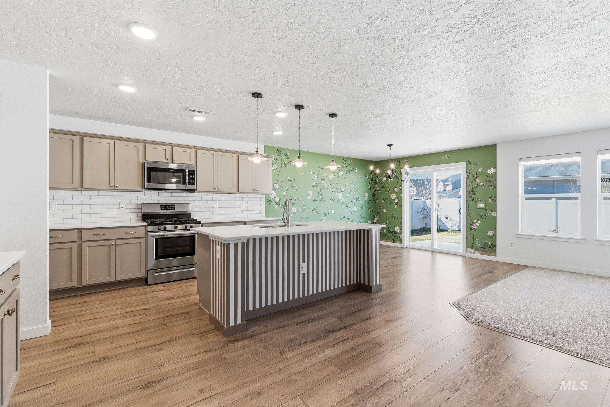 110 Homesteaders Street Middleton, ID 83644 - Photo 5 of 49 Kitchen featuring an island with sink, stainless steel appliances, a chandelier, light wood-style floors, and a textured ceiling