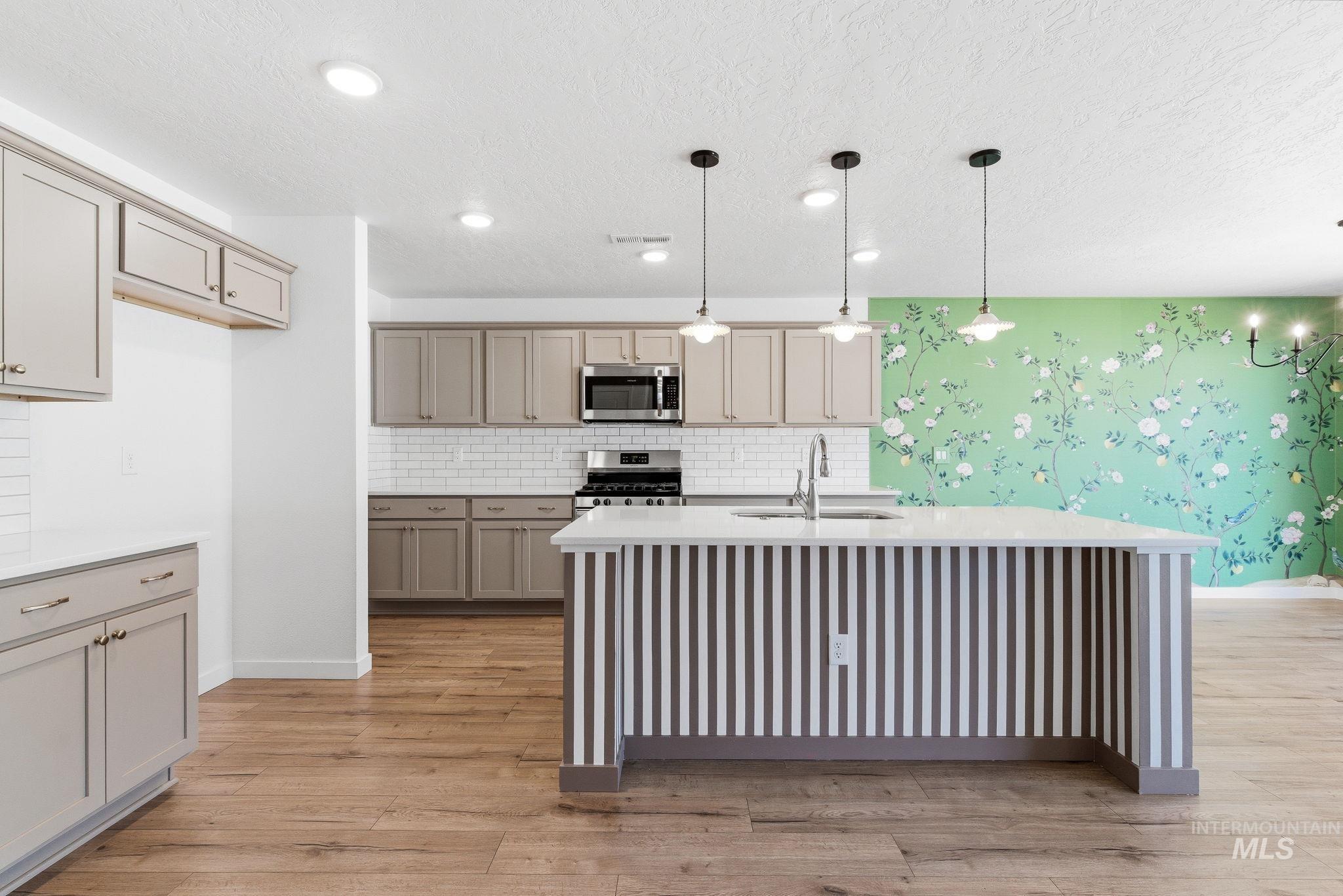 110 Homesteaders Street Middleton, ID 83644 - Photo 6 of 49 Kitchen with light stone countertops, light wood-type flooring, a center island with sink, decorative backsplash, and a textured ceiling