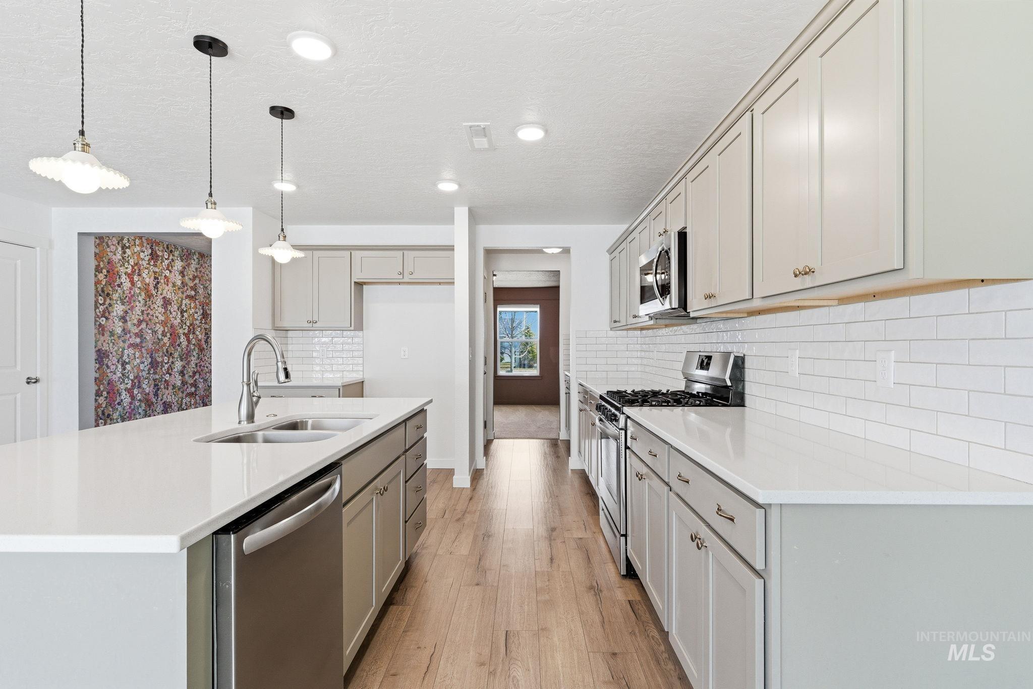 110 Homesteaders Street Middleton, ID 83644 - Photo 8 of 49 Two tone kitchen featuring stainless steel appliances, a kitchen island with sink, decorative light fixtures, light wood finished floors, and light stone countertops