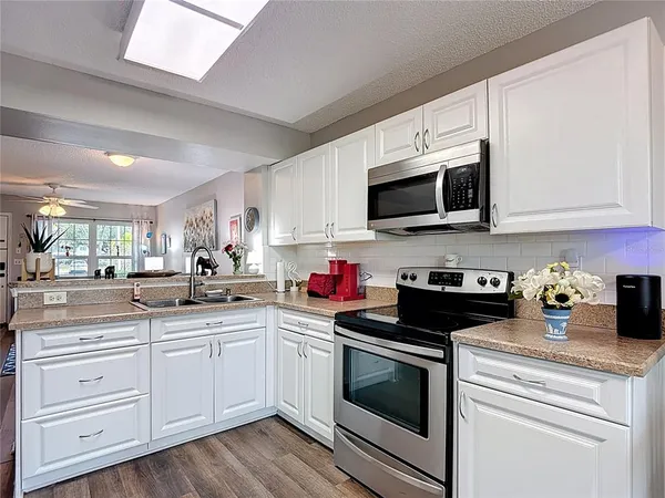 a kitchen with stainless steel appliances granite countertop a sink dishwasher a refrigerator and white cabinets with wooden floor