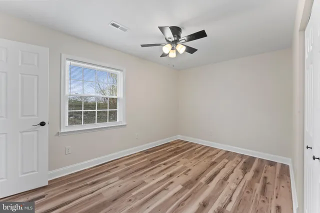 a view of empty room with wooden floor and fan