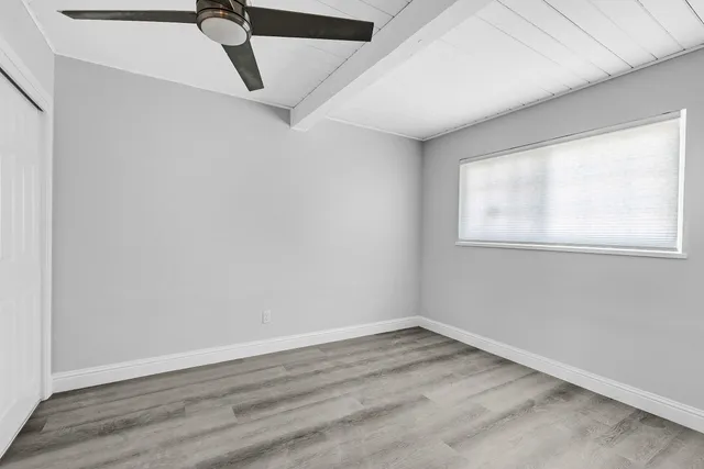 an empty room with wooden floor fan and windows