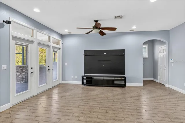 an empty room with wooden floor ceiling fan and windows