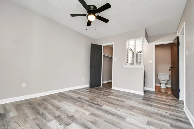 a view of an empty room with wooden floor and a ceiling fan