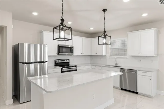 a kitchen with stainless steel appliances granite countertop a refrigerator a sink dishwasher a oven a dining table and chairs with wooden floors