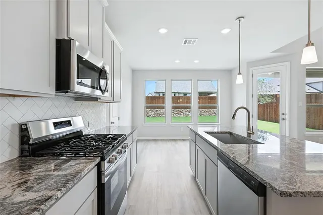 a large kitchen with stainless steel appliances granite countertop a large center island a stove a refrigerator and a cabinets