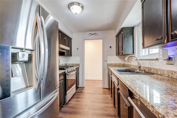 a kitchen with stainless steel appliances granite countertop a refrigerator a stove and a sink with wooden floor