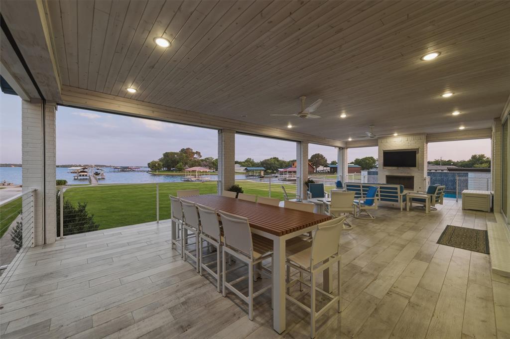6625 Sandy Beach Road Azle, TX 76020 - Photo 25 of 40 Covered patio includes outdoor dining and gathering areas with direct connection to the interior living spaces through sliding glass doors. Waterfront views extend across the lawn and shoreline areas beyond the covered exterior space.