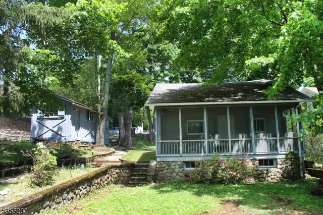 a view of house in front of a yard with potted plants and large trees