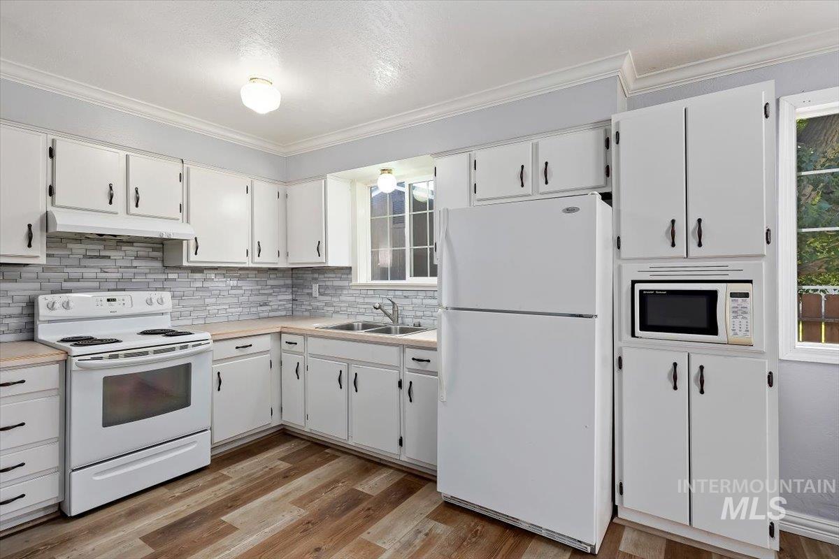 1940 Q Street Heyburn, ID 83336 - Photo 12 of 30 Kitchen featuring white cabinetry with dark hardware, a light-toned countertop, and a stacked stone-look backsplash