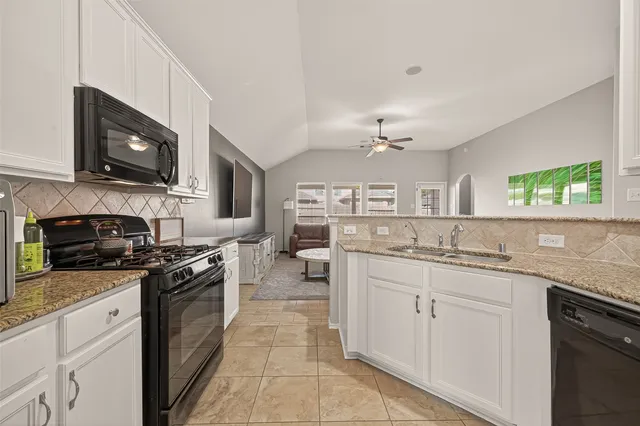 a kitchen with stainless steel appliances granite countertop a stove top oven a sink dishwasher and a microwave oven with white cabinets