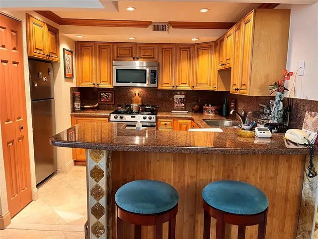 a kitchen with stainless steel appliances granite countertop a kitchen island stools a stove a sink dishwasher and microwave oven with wooden floor