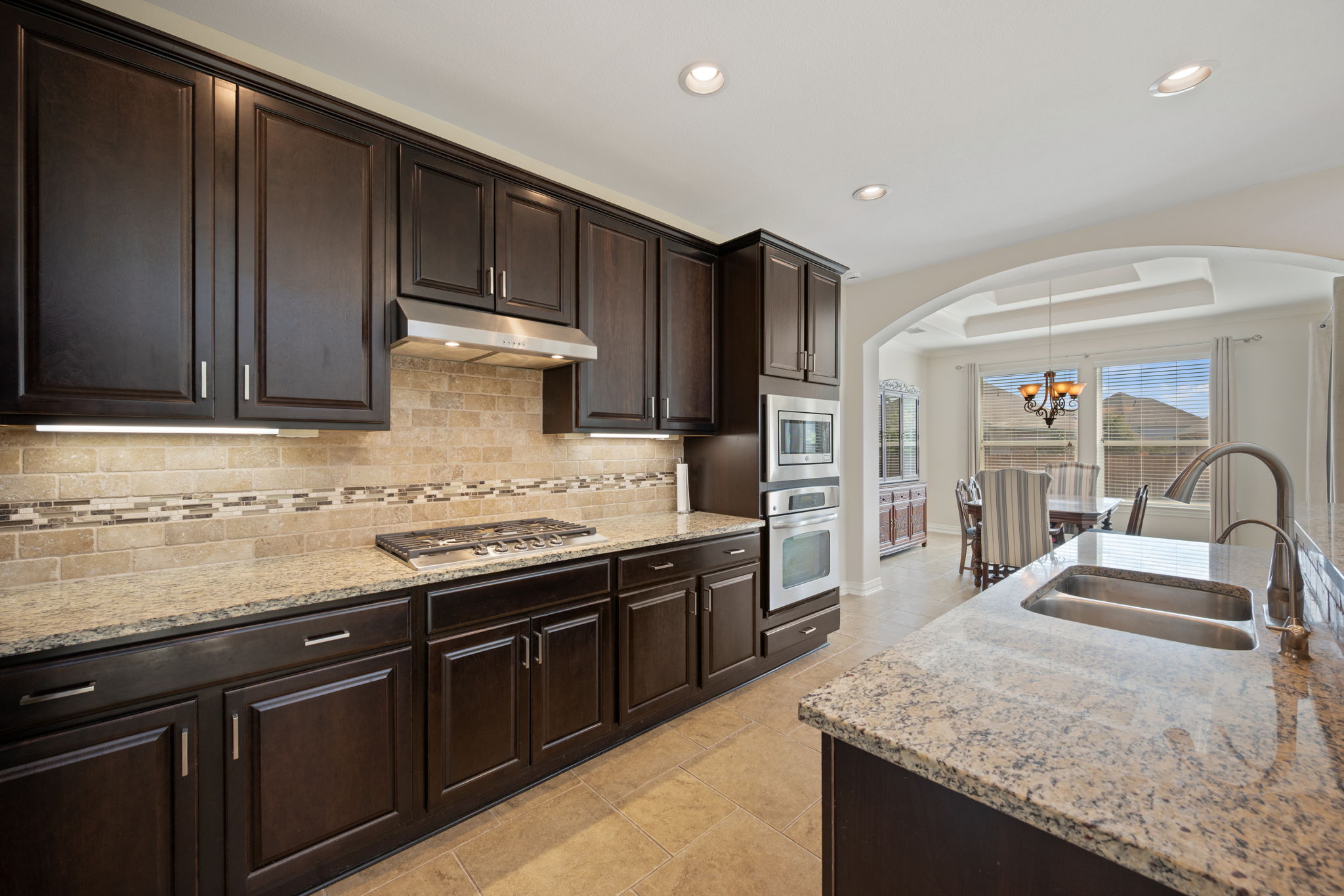 3904 Brean Down Road Pflugerville, TX 78660 - Photo 11 of 40 Kitchen with arched walkways, dark wood finish cabinets, light stone countertops, stainless steel appliances, and hanging lights