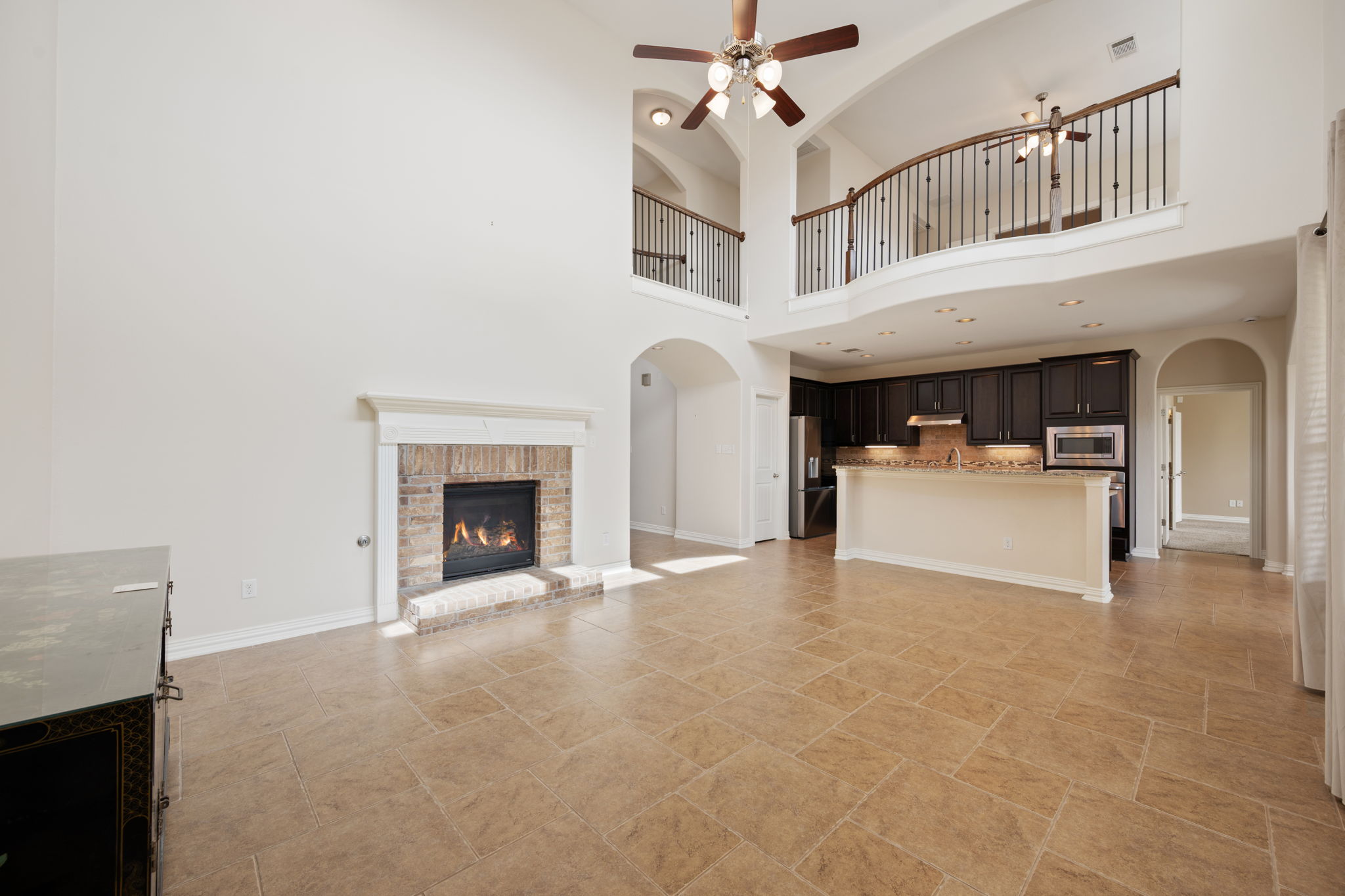 3904 Brean Down Road Pflugerville, TX 78660 - Photo 7 of 40 Unfurnished living room with arched walkways, a ceiling fan, a fireplace, a high ceiling, and light stone finish flooring