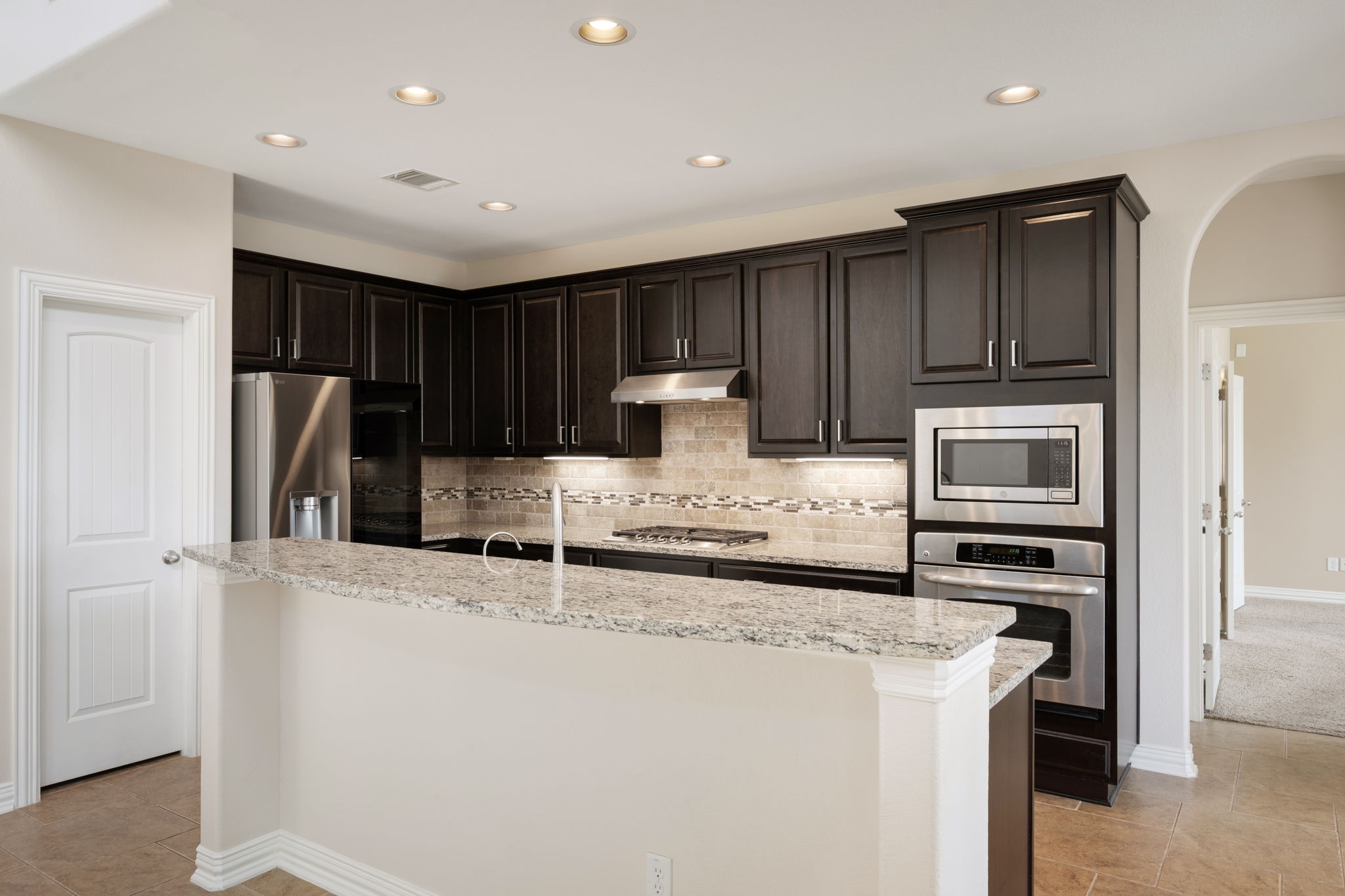3904 Brean Down Road Pflugerville, TX 78660 - Photo 8 of 40 Kitchen with arched walkways, decorative backsplash, stainless steel appliances, light stone counters, and dark wood finish cabinetry