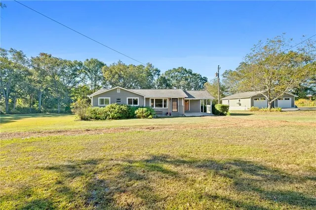 a white house with a big yard plants and large trees