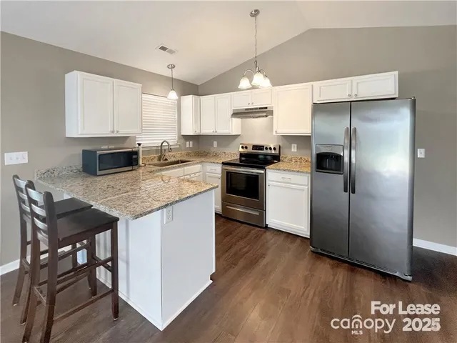 a kitchen with granite countertop a center island stainless steel appliances a refrigerator and a stove top oven