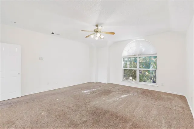 an empty room with chandelier fan and windows