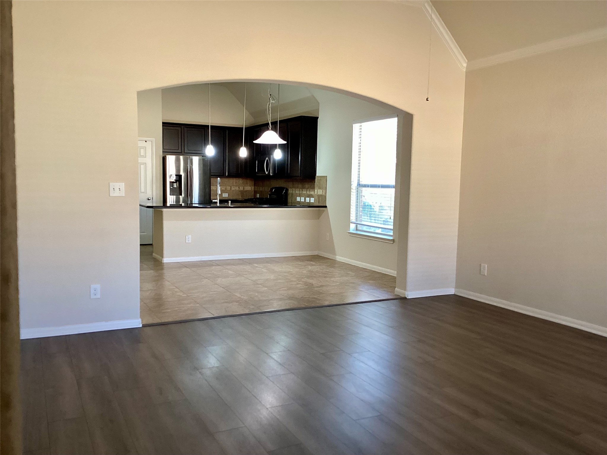 20122 Graphite Canyon Court Richmond, TX 77407 - Photo 18 of 27 Experience an open-concept living area with sleek laminate flooring, seamlessly connecting to a modern kitchen featuring dark cabinetry, stainless steel appliances, a breakfast bar, and abundant natural light from a large window.