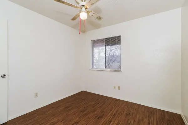 an empty room with wooden floor fan and windows