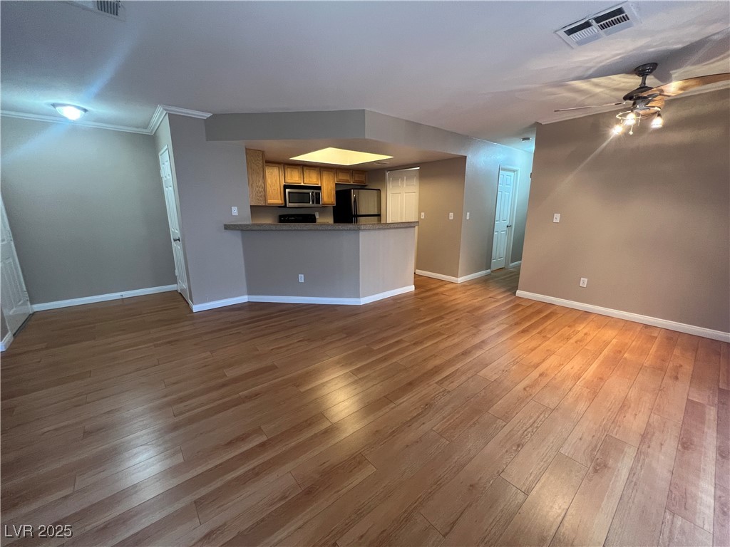 8600 West Charleston Boulevard, Unit 1060 Las Vegas, NV 89117 - Photo 4 of 14 Unfurnished living room featuring crown molding, a ceiling fan, and light wood-type flooring