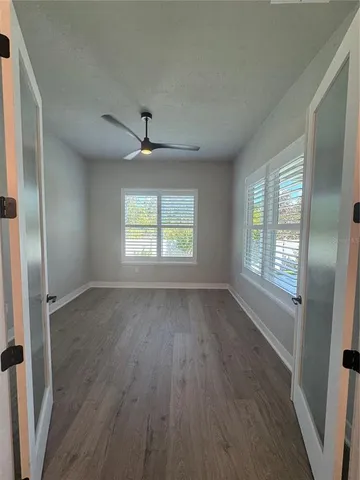 an empty room with wooden floor chandelier fan and windows