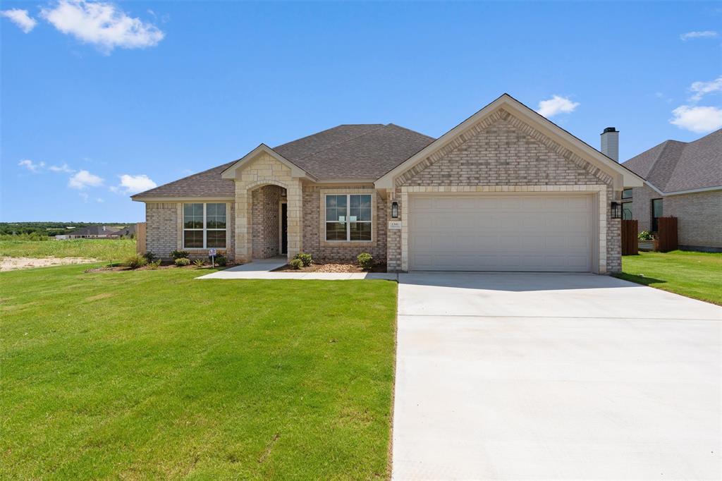 Traditional single-story home featuring a brick and stone facade, an attached two-car garage, a concrete driveway, and a manicured front lawn