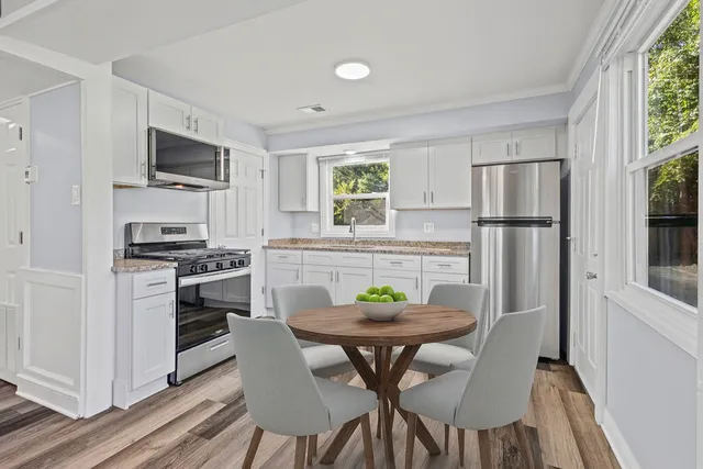 a kitchen with stainless steel appliances a refrigerator a stove a dining table and chairs with wooden floor