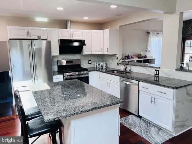 a kitchen with stainless steel appliances granite countertop a sink dishwasher a stove and a refrigerator with wooden floor