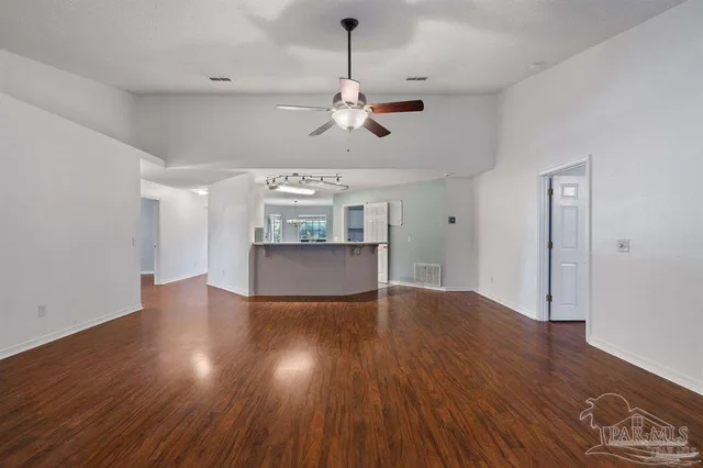 a view of an empty room with wooden floor and a ceiling fan