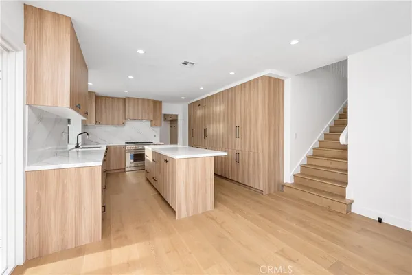a large kitchen with stainless steel appliances a large counter top a stove a sink dishwasher a refrigerator and a dining table with wooden floor