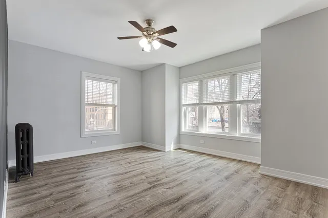 an empty room with wooden floor chandelier fan and windows