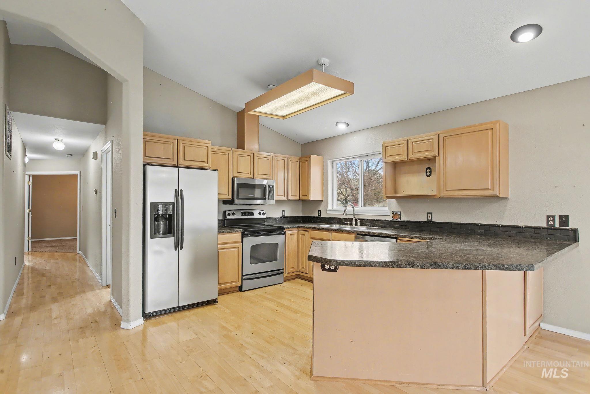 2242 Chukar Lane Clarkston, WA 99403 - Photo 12 of 41 Kitchen with appliances with stainless steel finishes, a peninsula, dark countertops, light brown cabinets, and vaulted ceiling