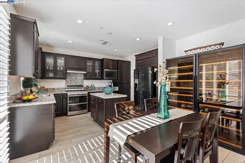 a kitchen with stainless steel appliances kitchen island granite countertop a refrigerator a stove a sink a dining table and chairs with wooden floor