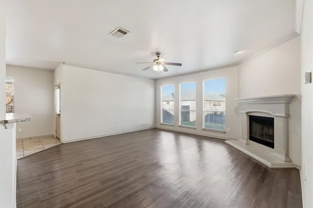 a view of an empty room with wooden floor and a kitchen