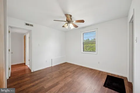 an empty room with wooden floor ceiling fan and windows