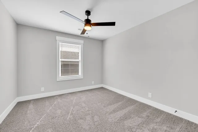 an empty room with chandelier fan and windows