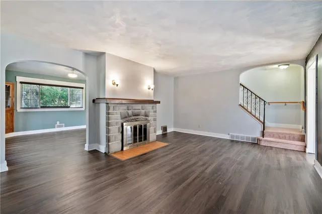 a view of an empty room with wooden floor fireplace and a window