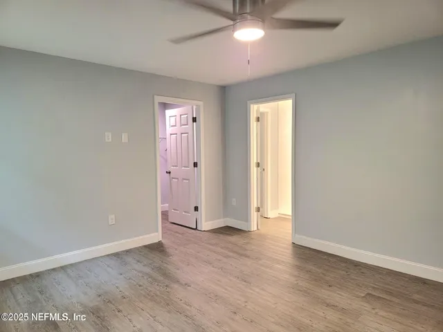 an empty room with wooden floor ceiling fan and windows