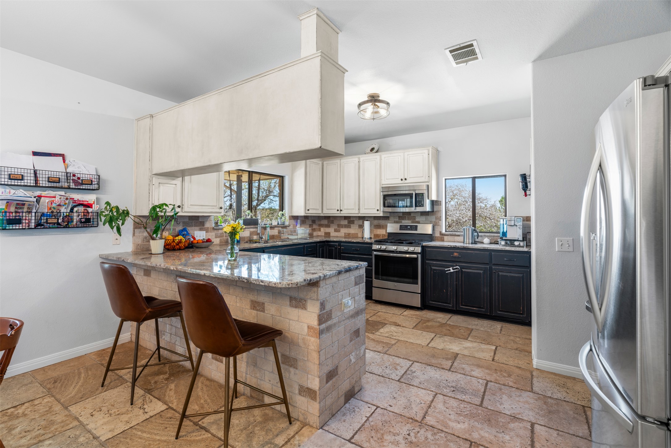 208 Amandas Way Leander, TX 78641 - Photo 5 of 25 Dual tone kitchen featuring stainless steel appliances, stone tile floors, a breakfast bar, a peninsula, and backsplash
