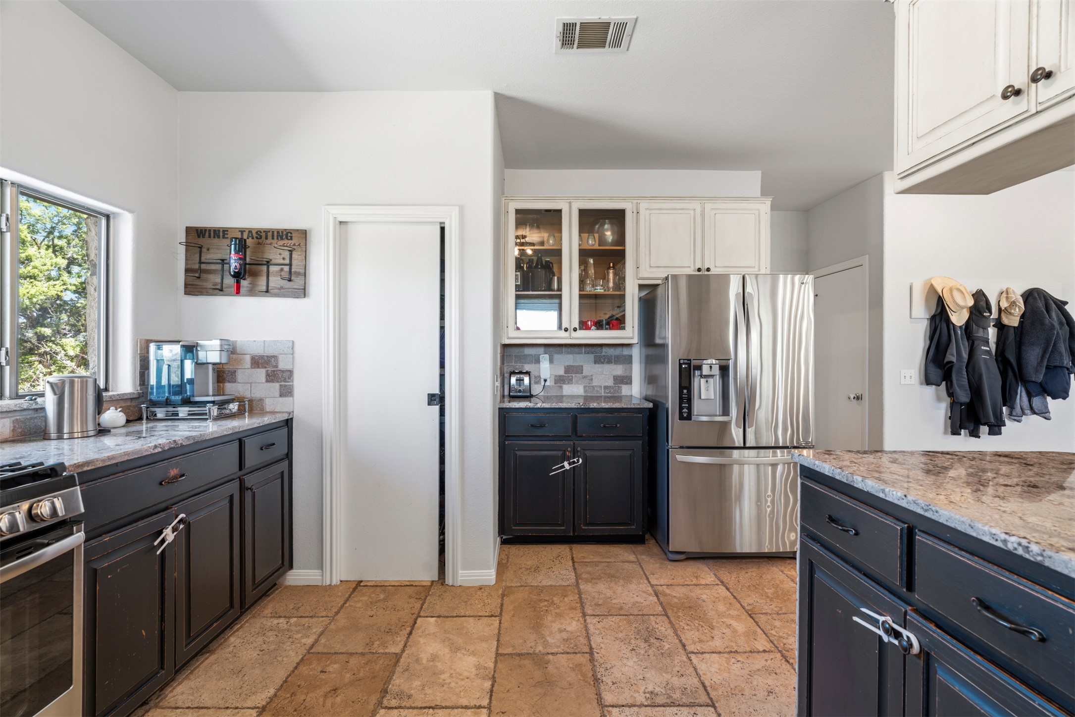 208 Amandas Way Leander, TX 78641 - Photo 8 of 25 Dual tone kitchen with light stone counters, stainless steel appliances, two tone cabinets, glass insert cabinets, and stone tile floors