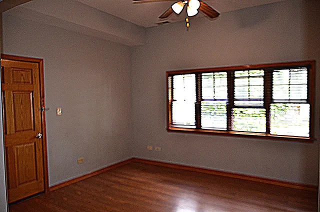 an empty room with wooden floor chandelier and windows
