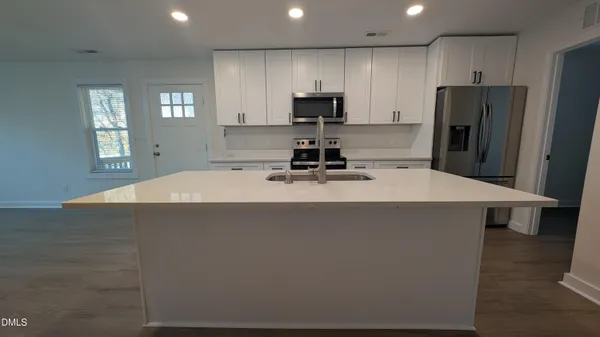 a view of an empty room and kitchen with wooden floor and a ceiling fan