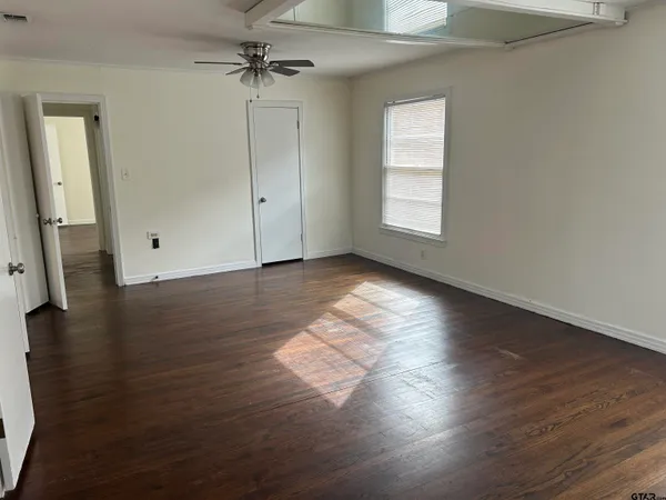 an empty room with wooden floor chandelier fan and windows