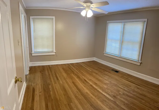 an empty room with wooden floor fan and windows